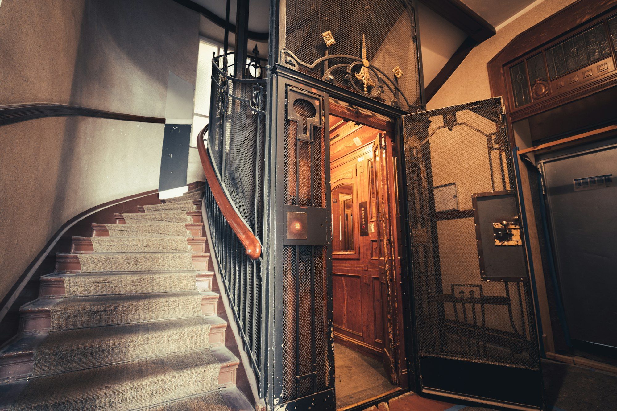 Altbau-Treppenhaus mit Holzstufen, schmiedeeisernem Geländer und historischem Aufzug
